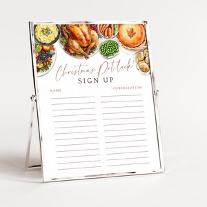 May include: A silver-framed Christmas potluck sign-up sheet. The top features watercolor illustrations of various dishes, including a roasted turkey, mashed potatoes, and pie. The sign reads "Christmas Potluck SIGN UP" with spaces for names and contributions.