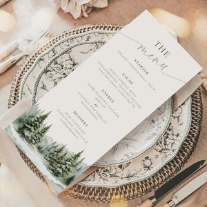 Puede incluir: Una tarjeta de menú blanca con una ilustración de acuarela de una escena de bosque nevado. El menú presenta un entrante, una ensalada, un plato principal y un postre. El texto del menú dice "The Menu", "Starter", "Creamy Tomato Basil Soup", "Salad", "Mixed Greens with Strawberries, Candied Pecans, and Balsamic Vinaigrette", "Entree", "Herb Roasted Chicken Breast", "Stuffed Portobello Mushrooms", "Dessert", "Mini Cupcakes Chocolate, Vanilla & Strawberry".