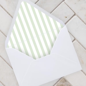 May include: A white envelope with a pale green and white striped lining. The envelope is open, displaying the striped pattern. The background is a light-coloured, textured surface.