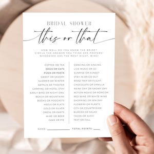 Puede incluir: Una tarjeta blanca con texto negro para un juego de despedida de soltera. La tarjeta dice "Bridal Shower This or That" e incluye una lista de opciones como "Café o té" y "Perros o gatos". La tarjeta está en manos de una persona.