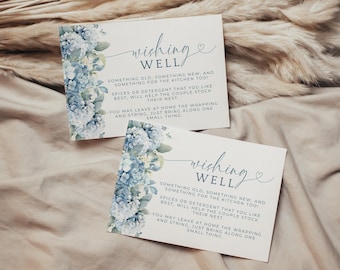 May include: Two white cards with the words "Wishing Well" in elegant script. The cards are decorated with blue and white hydrangea floral arrangements. The text on the cards suggests gift ideas for a couple.