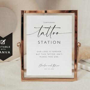 May include: A gold-coloured framed sign with the words "Temporary Tattoo Station" in elegant script. The sign includes the text "Our love is forever, but this tattoo isn't! Please take one." and the names "Charline and Mac" with a date.