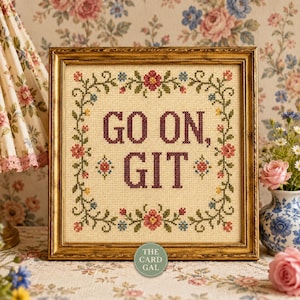 Puede incluir: Un bordado de punto de cruz cuadrado en un marco dorado que presenta el texto GO ON, GIT en letras de color rojo oscuro. El diseño está rodeado por un borde floral de enredaderas verdes, rosas rojas y pequeñas flores azules y amarillas sobre tela crema.