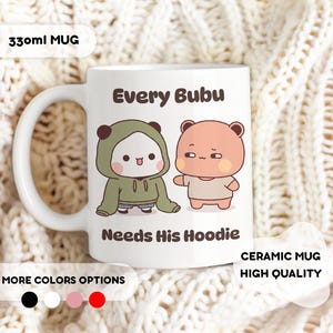 May include: White ceramic mug with the text "Every Bubu Needs His Hoodie" and illustrations of two cartoon characters. One character is wearing a green hoodie. The mug is labeled "330ml MUG" and "CERAMIC MUG HIGH QUALITY".
