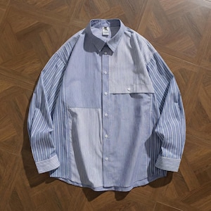 Può includere: Camicia a maniche lunghe con design patchwork. La camicia presenta un mix di tessuto blu chiaro a tinta unita e blu a righe verticali. Ha un colletto classico e una tasca sul petto.