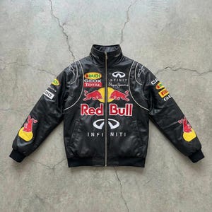 May include: Black leather jacket with a stand-up collar and a full-length zipper. The jacket features multiple sponsor logos, the Red Bull logo, and the Infiniti logo. White piping accents the design.