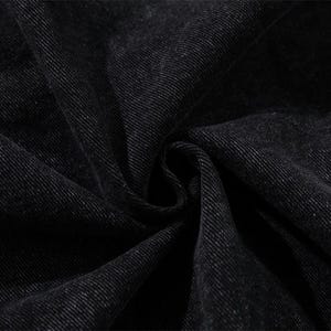 May include: Close-up of black denim fabric with visible texture and folds. The dark material has a subtle sheen, suggesting a garment or textile product. The image highlights the weave and color variations of the fabric.