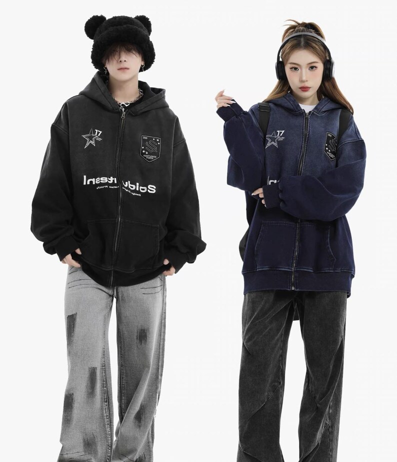 May include: Two people wearing matching zip-up hoodies and jeans. One hoodie is black, the other is navy blue. Both hoodies have a star and shield emblem, and the text "Investiblos". The jeans are gray and black.