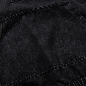 May include: Close-up of a black denim hoodie pocket. The pocket is large and rectangular, with visible stitching around the edges. The fabric has a slightly faded appearance, suggesting a worn or washed look. The hoodie's elastic waistband is visible.