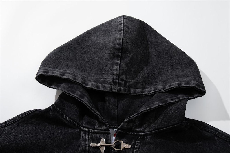 May include: Close-up of a black denim hooded jacket. The jacket features a hood, a metal toggle closure, and a faded, distressed appearance. The fabric appears to be a dark wash denim.