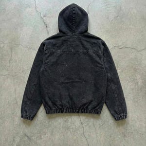 May include: A black hooded jacket with a faded, textured appearance. The jacket features a drawstring hem and cuffs, and a full-length zipper. The back view shows the hood and the seam details.