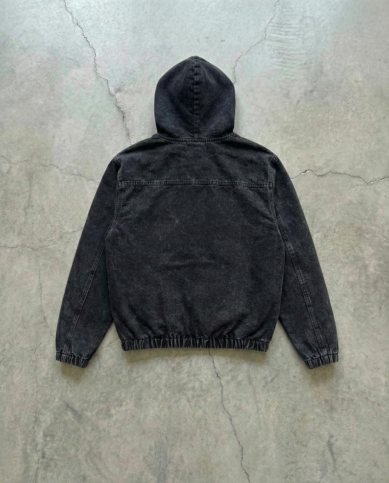 May include: A black hooded jacket with a faded, textured appearance. The jacket features a drawstring hem and cuffs, and a full-length zipper. The back view shows the hood and the seam details.