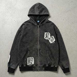 Peut inclure: Un sweat à capuche zippé gris anthracite avec un aspect délavé et texturé. Le sweat à capuche est doté d'une capuche, d'une poche avant et de poignets et d'un ourlet côtelés noirs. Des écussons avec des portraits en noir et blanc sont cousus sur le devant et la manche.