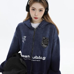 May include: A dark blue zip-up hoodie with white text and patches. The hoodie features a faded design, a front zipper, and a hood. The patches include the text "INS" and "INSTUDIOS FIRST".