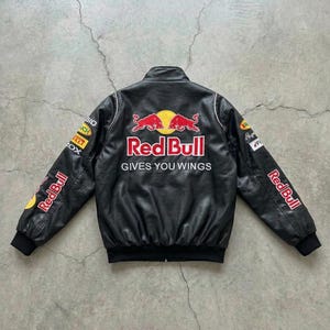 May include: Black leather jacket with Red Bull logos and text. The jacket features white trim, black cuffs, and the phrase "GIVES YOU WINGS" on the back. Logos are on the sleeves and chest.