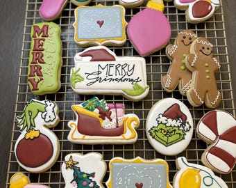 Puede incluir: Una colección de galletas navideñas dispuestas sobre una rejilla. Las galletas presentan varias formas festivas, incluyendo adornos, un árbol de Navidad, un trineo y hombres de jengibre. Los colores incluyen rosa, verde, rojo y blanco.