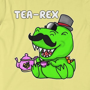 Può includere: Una maglietta gialla con un dinosauro verde che indossa un cappello a cilindro, occhiali da sole e baffi. Il dinosauro tiene una tazza da tè e una teiera. Il testo "TEA-REX" è stampato sulla maglietta.