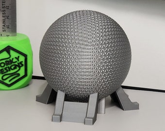 Könnte beinhalten: Ein graues 3D-gedrucktes Modell von Spaceship Earth, der ikonischen geodätischen Kugel in Epcot, mit einem Sockel. Das Modell steht auf einer weißen Oberfläche.