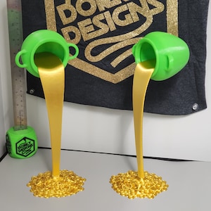 Puede incluir: Dos ollas verdes con líquido dorado que se derrama de ellas. El líquido forma una pila de monedas de oro en el fondo de cada olla.