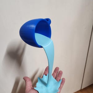 Puede incluir: Una taza de té azul parece estar vertiendo un líquido azul claro en un chapoteo estilizado. La taza de té tiene un asa y está inclinada, con el líquido fluyendo hacia abajo. El chapoteo se sostiene en una mano.