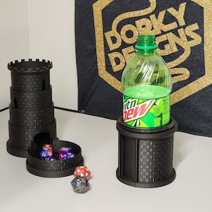 May include: Two black 3D printed towers with a brick pattern. One tower has a round opening at the bottom and is holding several dice. The other tower has a round opening at the top and is holding a green plastic bottle. The bottle has a white label with the text "Mountain Dew" on it. The towers are on a white surface.