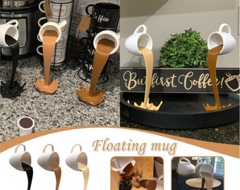 May include: Three white ceramic mugs with brown liquid pouring out of them. The mugs are tilted upside down and the liquid is frozen in mid-air. The text "But first, coffee!" is on a black sign behind the mugs. The caption "Floating mug" is below the image.
