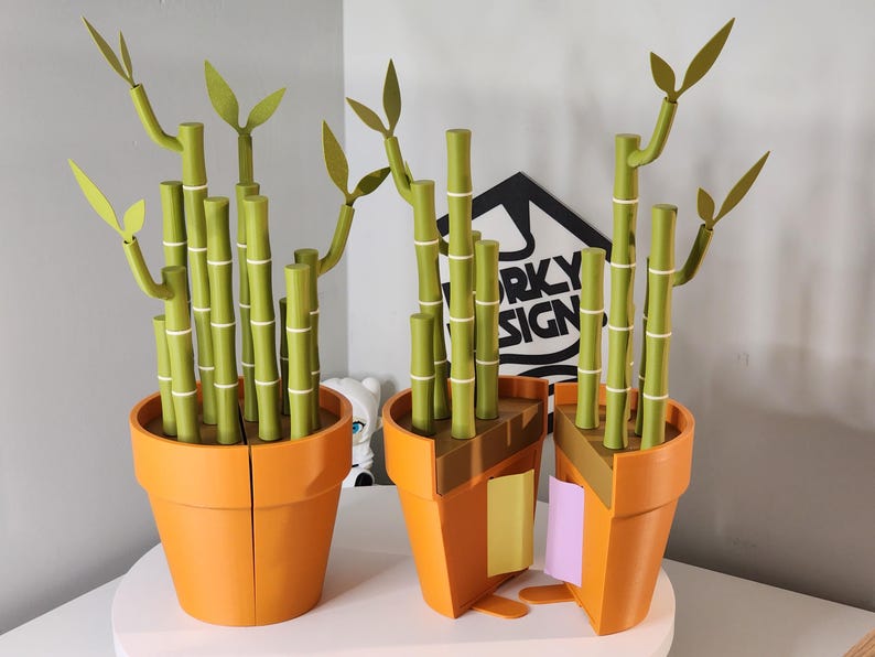 Peut inclure: Deux pots de fleurs oranges contiennent chacun un plant de bambou. Les tiges de bambou sont vertes avec des bandes blanches, et les feuilles sont vert clair. Un pot est coup&eacute;, r&eacute;v&eacute;lant l'int&eacute;rieur. Le fond comprend une enseigne avec "FUNKY DESIGN".