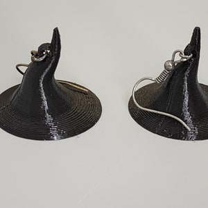 May include: A pair of black witch hat earrings with silver and gold hooks. The hats are 3D printed and have a textured surface.