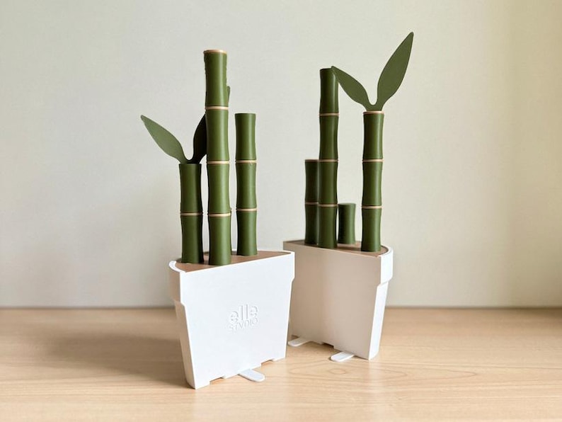 Peut inclure: Deux plantes de bambou d&eacute;coratives dans des pots blancs. Les tiges de bambou sont vertes avec des accents dor&eacute;s, et les feuilles sont vert fonc&eacute;. Les pots sont rectangulaires avec un design minimaliste.