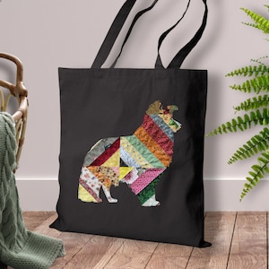 May include: Black tote bag featuring a colorful patchwork dog design. The dog silhouette is composed of various fabric patterns in shades of red, yellow, green, and blue. The bag has black handles and is displayed indoors.
