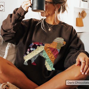 May include: Dark chocolate brown sweatshirt featuring a patchwork dog design. The dog silhouette is composed of various fabric patterns and colors, including floral, striped, and solid textures. The text "Dark Chocolate" is at the bottom.