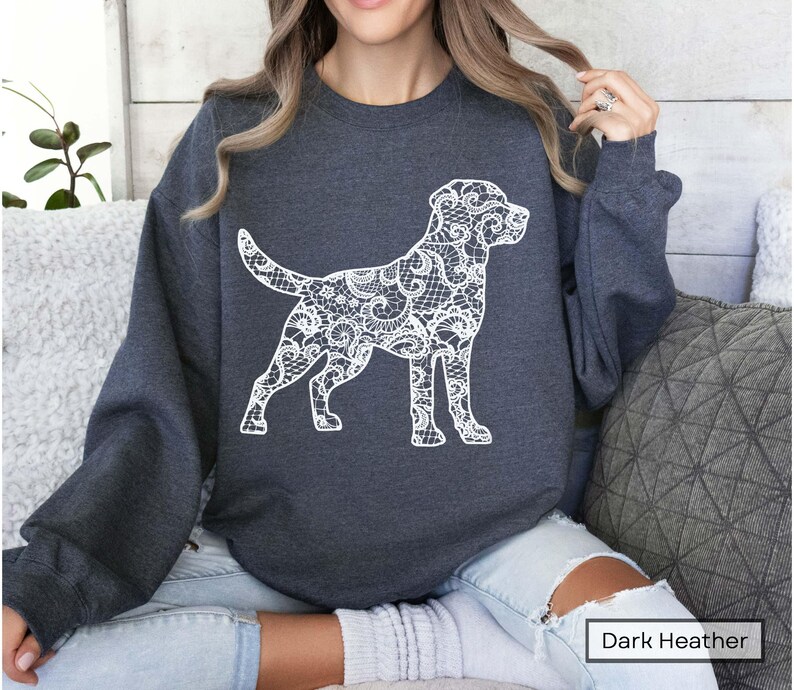May include: Dark heather gray sweatshirt featuring a white lace-patterned dog silhouette. The dog design is detailed and stands out against the dark background. The sweatshirt is a casual style, suitable for everyday wear.