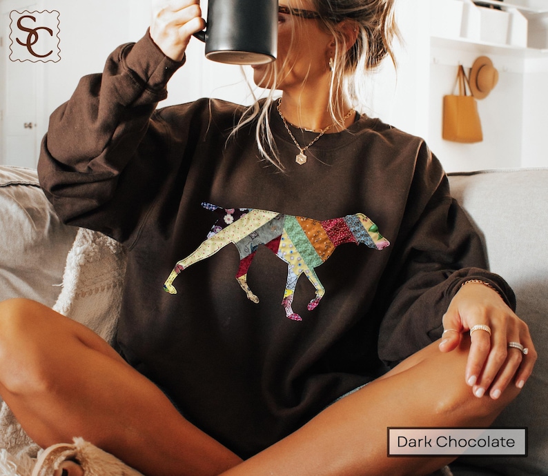 May include: Dark chocolate brown sweatshirt with a patchwork dog design. The dog silhouette is made up of various fabric patterns and colours, including red, blue, yellow, and green. The text "Dark Chocolate" is at the bottom.