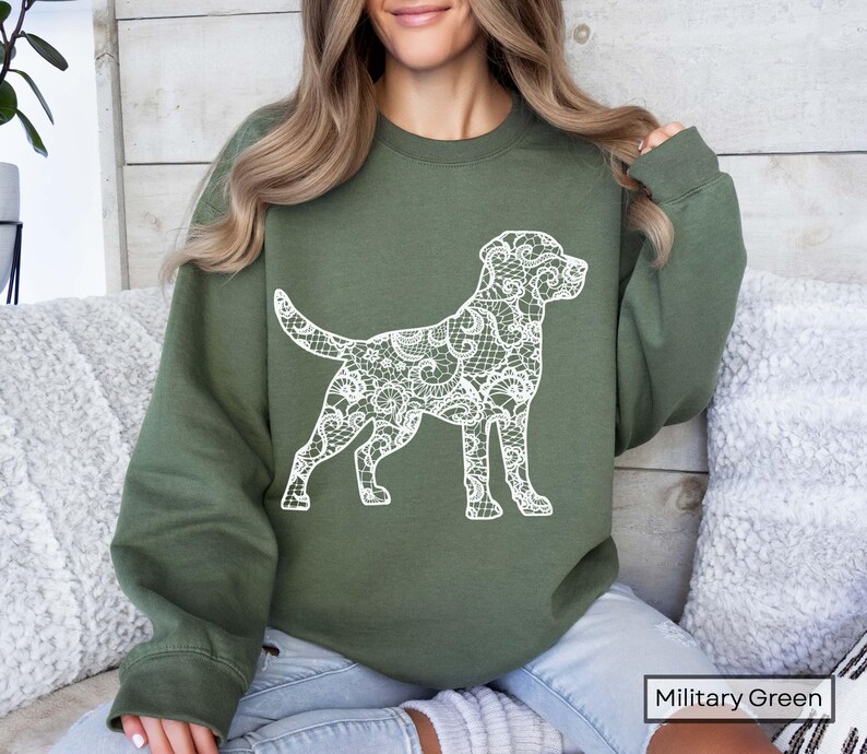 May include: Military green sweatshirt featuring a white lace-patterned dog silhouette. The dog design is detailed and covers the entire body of the dog. The sweatshirt is a solid color and has a crew neck.