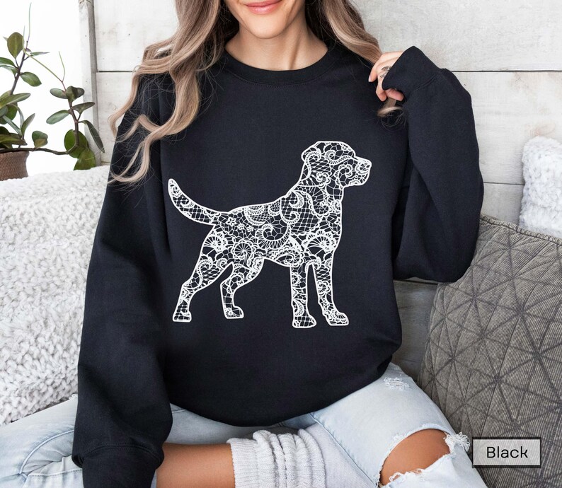 May include: Black sweatshirt featuring a white dog silhouette with a lace-like design. The dog is in a standing pose, with its tail up. The sweatshirt is a solid black color.
