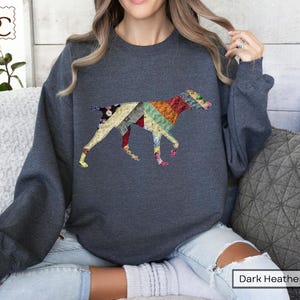 May include: Dark heather grey sweatshirt with a patchwork dog design. The dog is made of various fabric patterns in red, yellow, green, and blue. The sweatshirt has a crew neck and long sleeves.