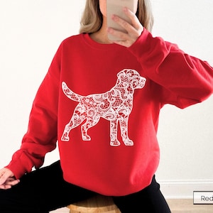 May include: A red sweatshirt featuring a white lace-patterned dog design. The dog is standing, with its tail up and head turned slightly to the side. The sweatshirt is a solid red color, and the dog design is a detailed, intricate pattern.