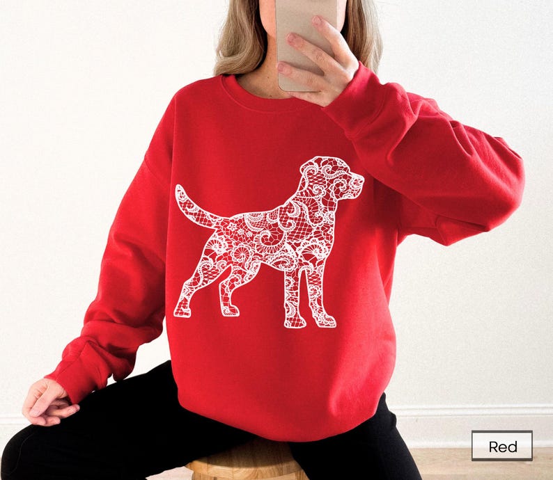 May include: A red sweatshirt featuring a white lace-patterned dog design. The dog is standing, with its tail up and head turned slightly to the side. The sweatshirt is a solid red color, and the dog design is a detailed, intricate pattern.
