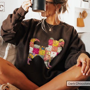 May include: A dark chocolate brown long-sleeve sweatshirt featuring a large, central graphic of a dog silhouette filled with a colorful, multi-patterned patchwork quilt design consisting of floral, paisley, and geometric prints in various bright colors.