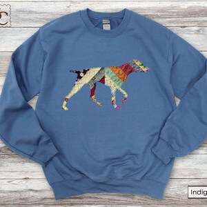 May include: Indigo blue sweatshirt with a colourful patchwork dog design. The dog silhouette is made up of various fabric patterns in shades of red, yellow, green, and blue. The sweatshirt has a crew neck and long sleeves.