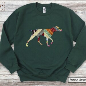 May include: A forest green sweatshirt with a patchwork dog design. The dog is made up of colourful fabric patterns in red, yellow, blue, and green. The sweatshirt has a crew neck and long sleeves. The text "Forest Green" is at the bottom.