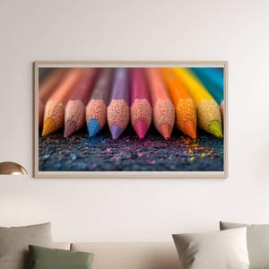 Puede incluir: Primer plano de una impresión artística enmarcada que presenta una fila de lápices de colores afilados en varios tonos, incluyendo amarillo, naranja, rosa, morado y azul. Los lápices están dispuestos sobre una superficie oscura con polvo de pigmento colorido.