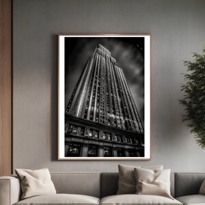 May include: Black and white photograph of a tall skyscraper in the city. The building is viewed from a low angle, looking up at the top of the building. The sky is cloudy and the building is illuminated by the sun.