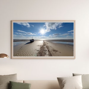 Puede incluir: Un barco solitario se encuentra en una playa de arena con el sol brillando intensamente en el cielo azul. La marea está baja, revelando la arena y el reflejo del barco en el agua.