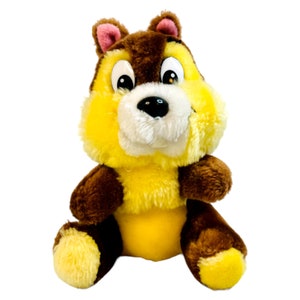 Puede incluir: Un juguete de peluche de una ardilla de dibujos animados con orejas marrones, pelaje marrón y vientre amarillo. La ardilla tiene un hocico blanco y ojos negros.