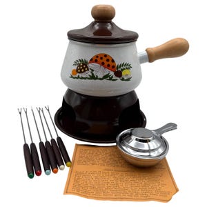 Puede incluir: Un juego de fondue vintage con una olla marrón y blanca con ilustraciones de setas. El juego incluye un soporte, un quemador, seis tenedores de fondue con puntas de colores y un pequeño cucharón de metal. La olla tiene un asa y una tapa de madera.