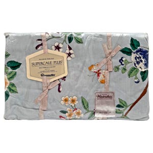 Puede incluir: Una sábana encimera azul claro empaquetada en plástico, con un estampado floral de flores blancas, azules y naranjas y hojas verdes. Una etiqueta dice No-Iron Percale Supercale Plus 200 Thread Count Queen Flat Sheet Wamsutta Winterthur.