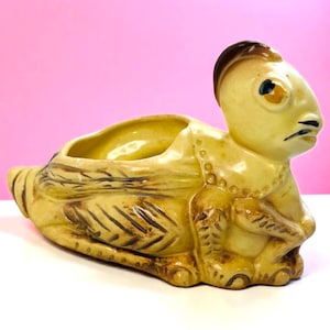 Könnte beinhalten: Ein Vintage-Keramik-Pflanzgefäß in Form einer Heuschrecke. Der Pflanztopf ist überwiegend gelb mit braunen Akzenten, einschließlich der Beine, Flügel und Kopf des Insekts. Die Heuschrecke hat ein detailliertes Gesicht und eine große Öffnung.