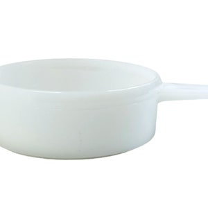 May include: White ceramic ramekin with a handle. The ramekin is round and has a smooth, glossy finish.