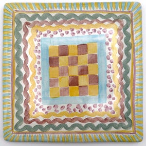 May include: Square decorative plate with a hand-painted design. The plate features a checkerboard pattern in the center, surrounded by layers of colorful borders in yellow, blue, green, and purple. The edges have a striped pattern.
